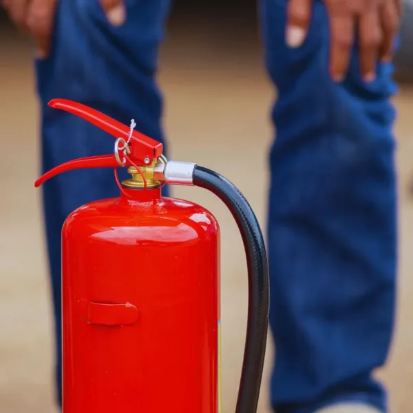Closeup image of fire extinguisher with a blured vision of pair legs seen in the rear.