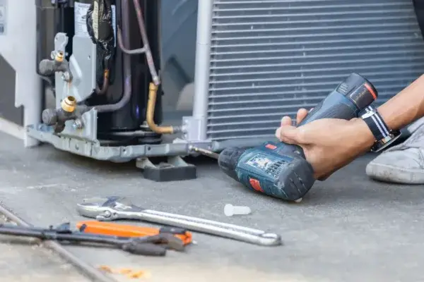 A man seen un screwing HVAC unit with tools spreading on the ground.